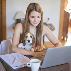 A young woman using a laptop at home with her beagle on her lap.