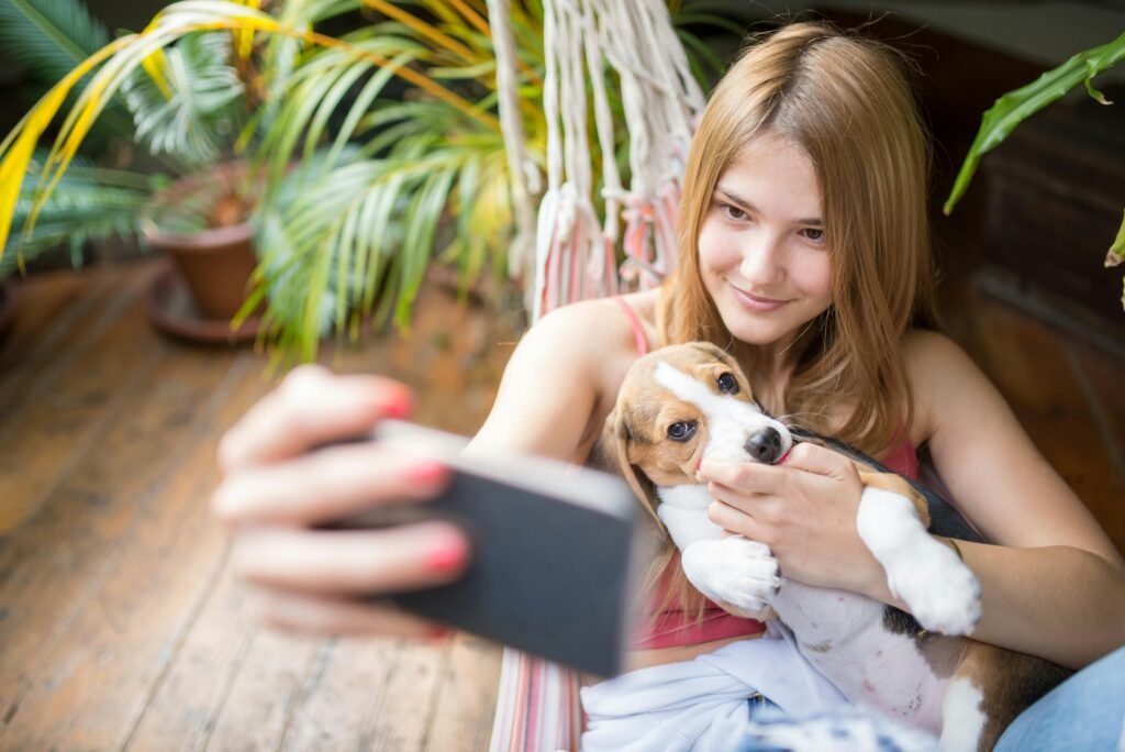 A smiling woman cuddles her cute beagle puppy while taking a selfie in a hammock.